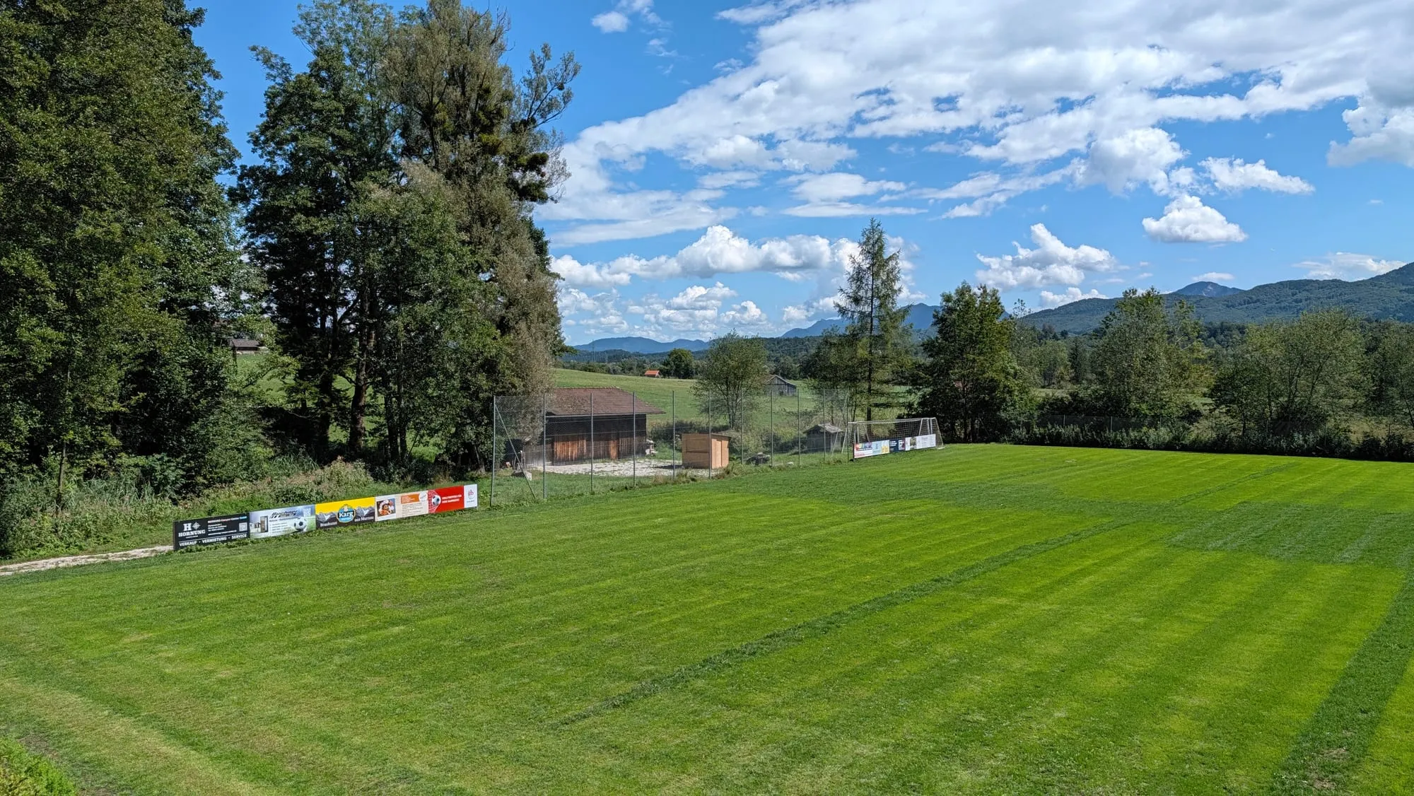 Der Fußballplatz mit Blick auf das Tor, die Bandenwerbung und die Berge im Hintergrund