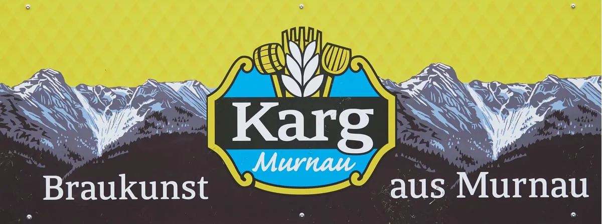 Bandenwerbung der Brauerei Karg mit einer Bergkette und dem Schriftzug „Braukunst aus Murnau“